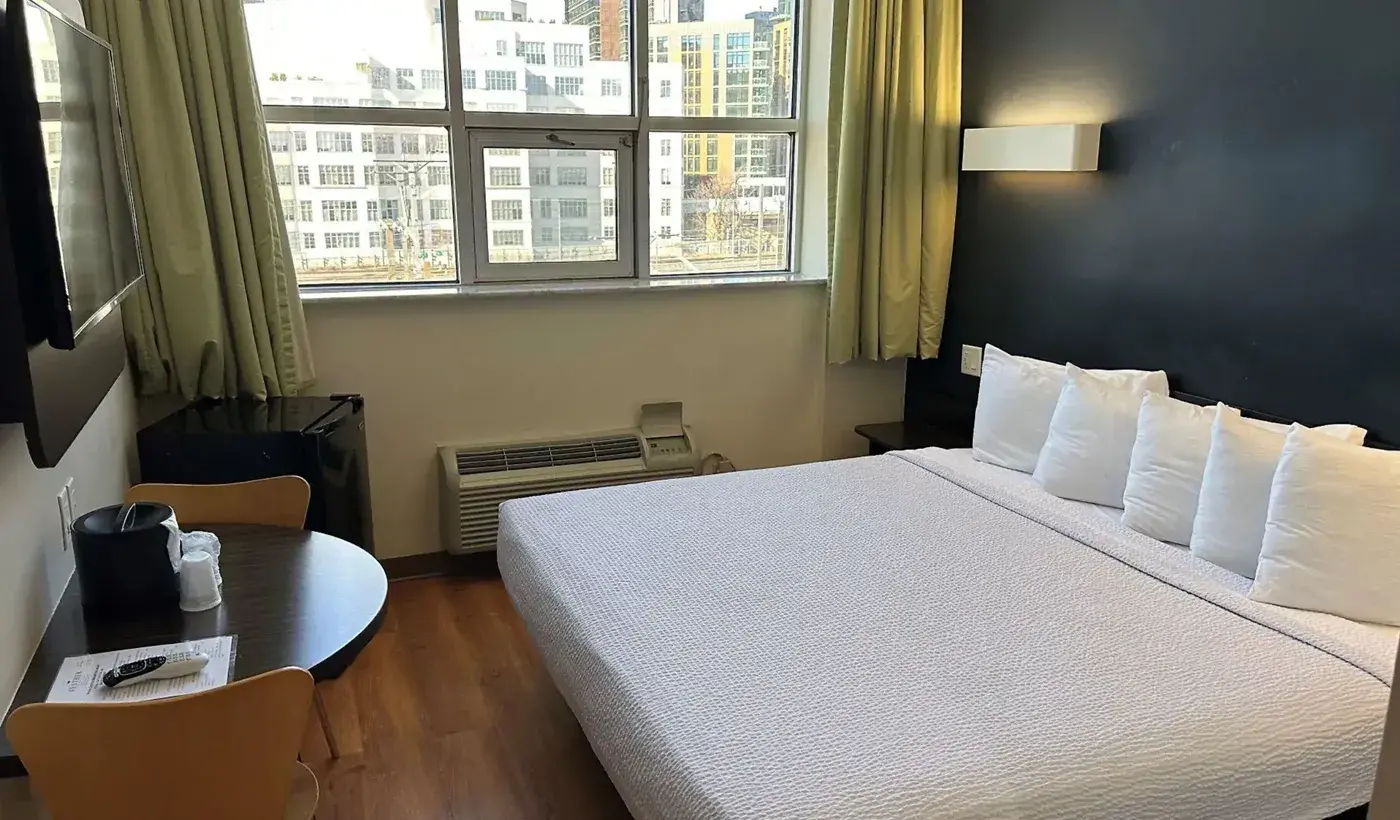 Queen Room im Feather Factory Hotel mit rundem Tisch und großem Fenster zu den Gebäuden der Stadt