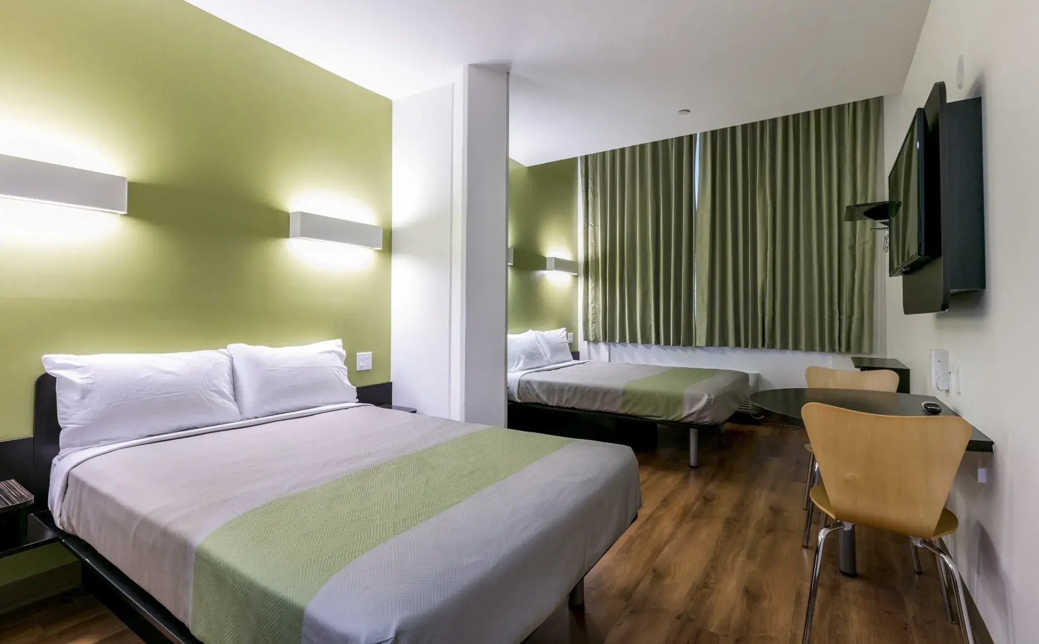 Zimmer mit zwei durch eine Säule getrennten Betten, Tisch mit Stühlen und Flachbildfernseher