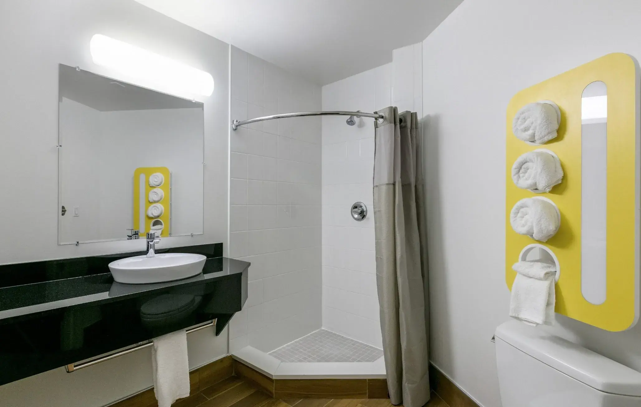 Badezimmer mit Dusche, Waschbecken auf schwarzer Ablage und gelbem Handtuchhalter